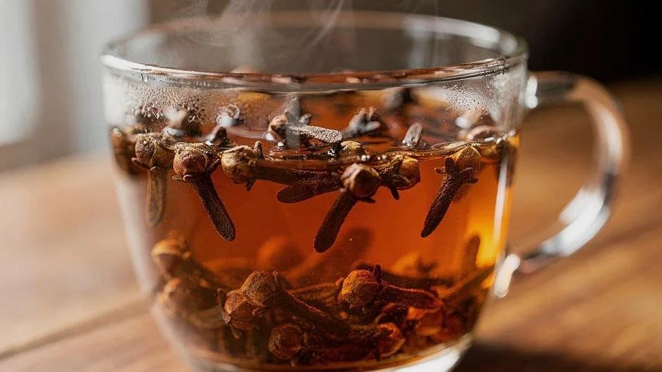 Tazza di vetro con infuso caldo di chiodi di garofano e vapore che sale